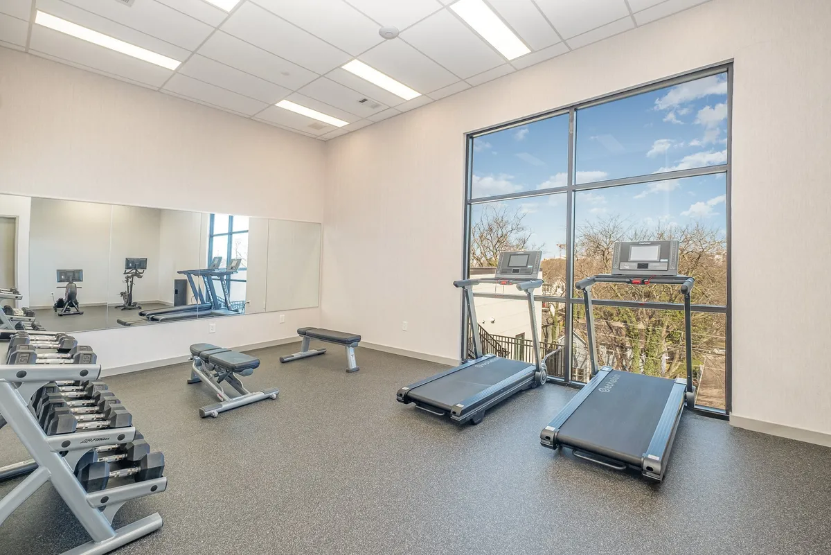 A bright, modern gym equipped with treadmills, weight benches, and a mirrored wall. The inviting space is designed for both cardio and strength training, catering to solo or group workouts.