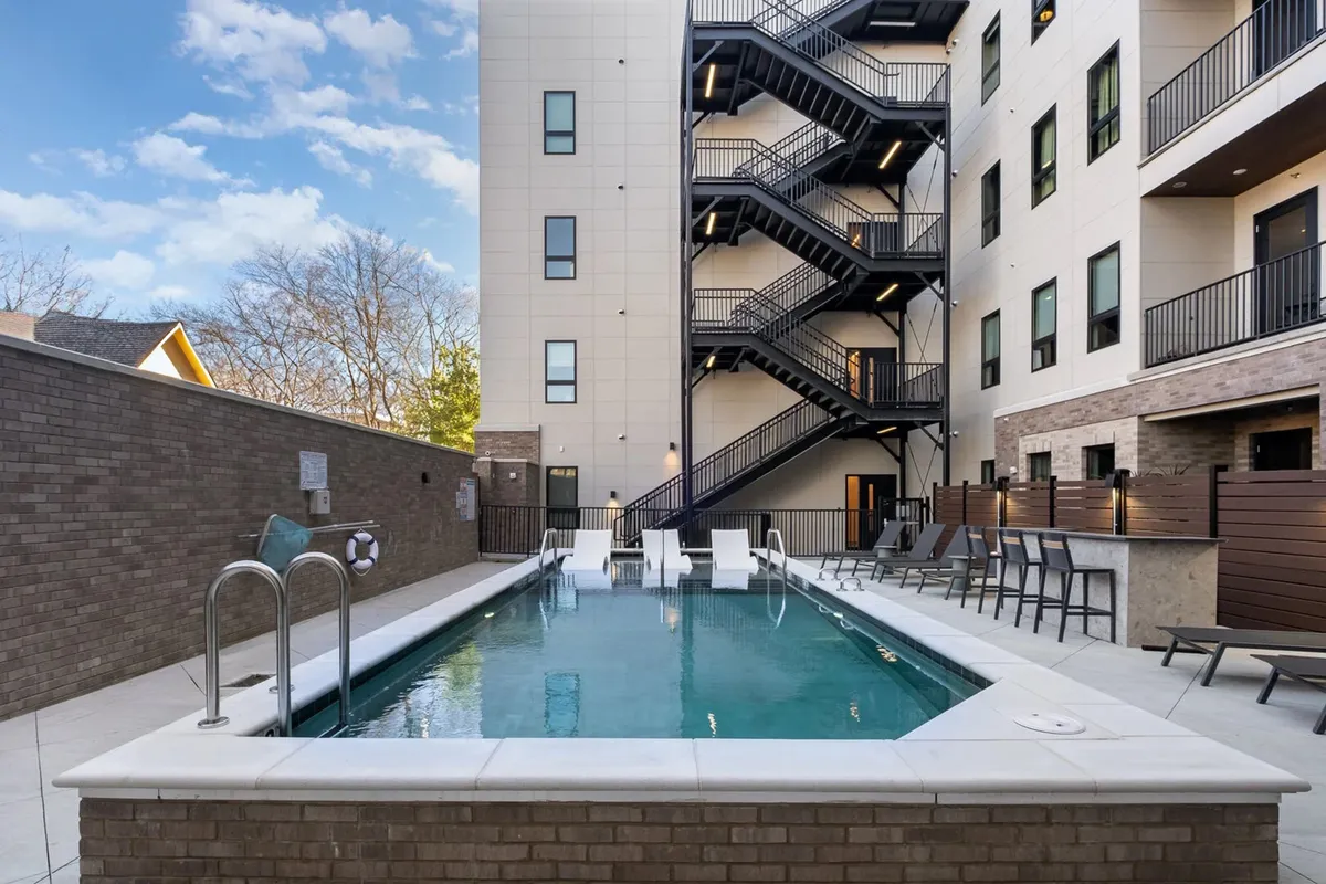 A sparkling swimming pool surrounded by comfortable outdoor seating and a stairway leading to a lounge area. The setting exudes a relaxed and social atmosphere, ideal for sunbathing or enjoying a drink with friends.