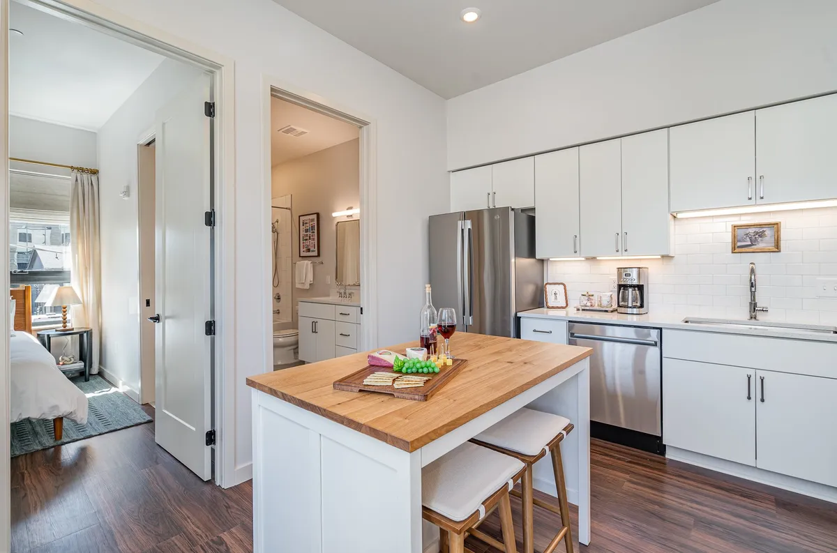 A contemporary kitchen scene with a kitchen island set for snacks and drinks, gleaming stainless steel appliances in the background, and a bright countertop. The space feels lively, open, and designed for casual dining or hosting gatherings.