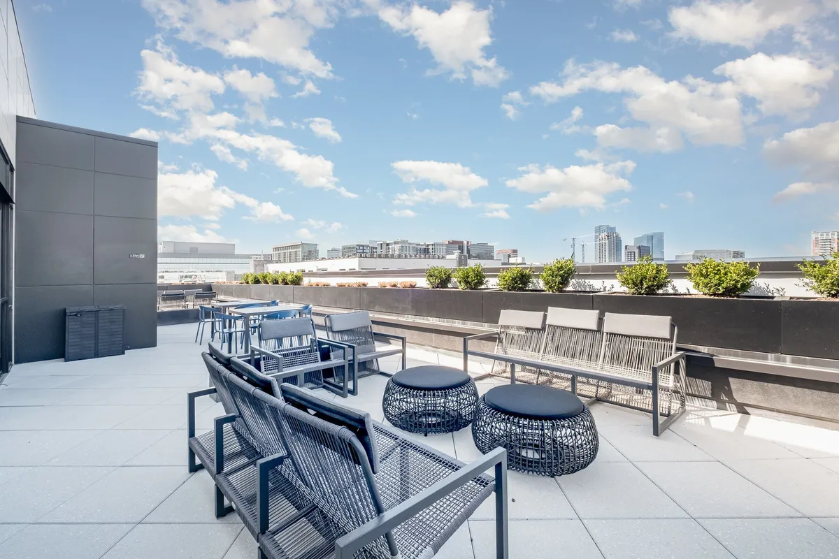 This exterior image features a modern rooftop lounge area with comfortable seating, lush planters, and an urban skyline in the background. The rooftop is designed for social gatherings, relaxation, and enjoying expansive city views, both during the day and at sunset. The mood is contemporary and relaxed, perfect for unwinding above the vibrant city below.