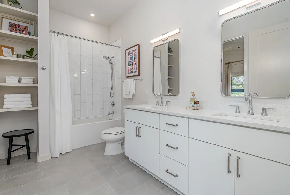 A spacious bathroom with a double sink vanity, mirrors, elegant lighting, and a glass-enclosed shower, all accentuated by soft decor and a refreshing, spa-like ambiance.