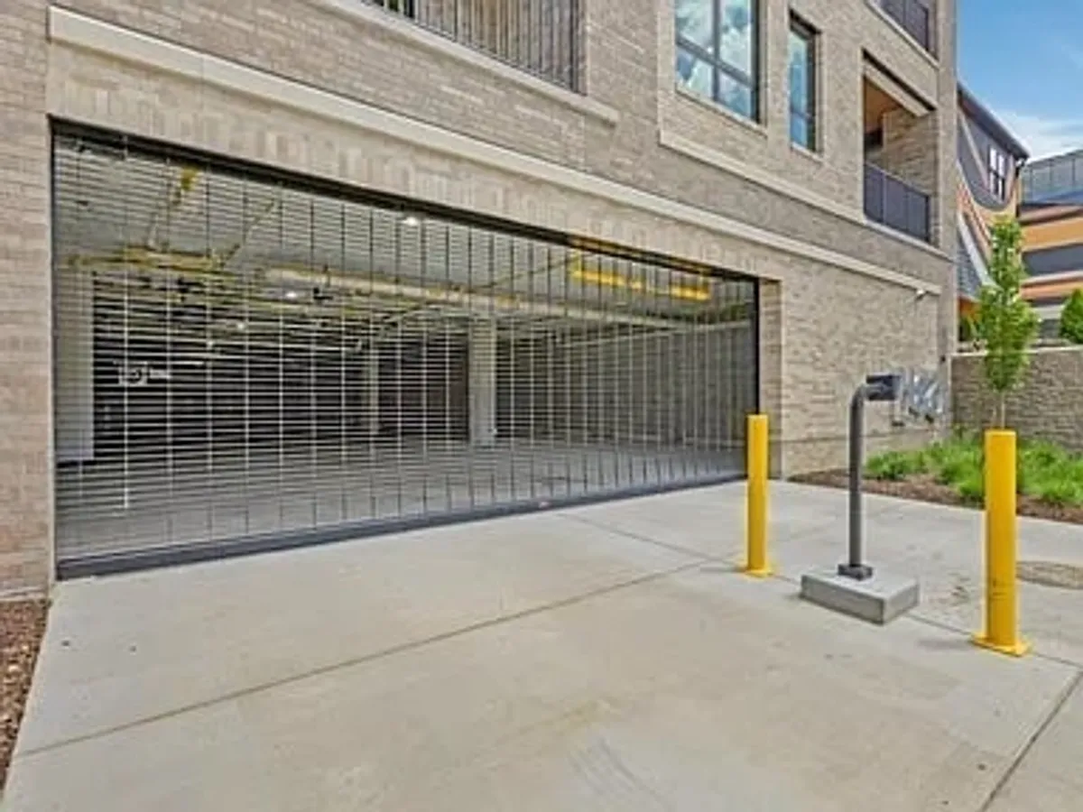 A secure parking garage with a roller shutter door, yellow bollards, and a smooth concrete surface. The clearly marked space signals safety and easy access for vehicles, including EVs.
